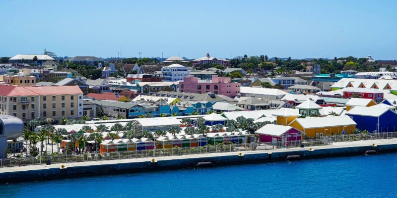 Waterfront view of a colorful coastal town with bright buildings, palm trees, and blue water in the foreground.